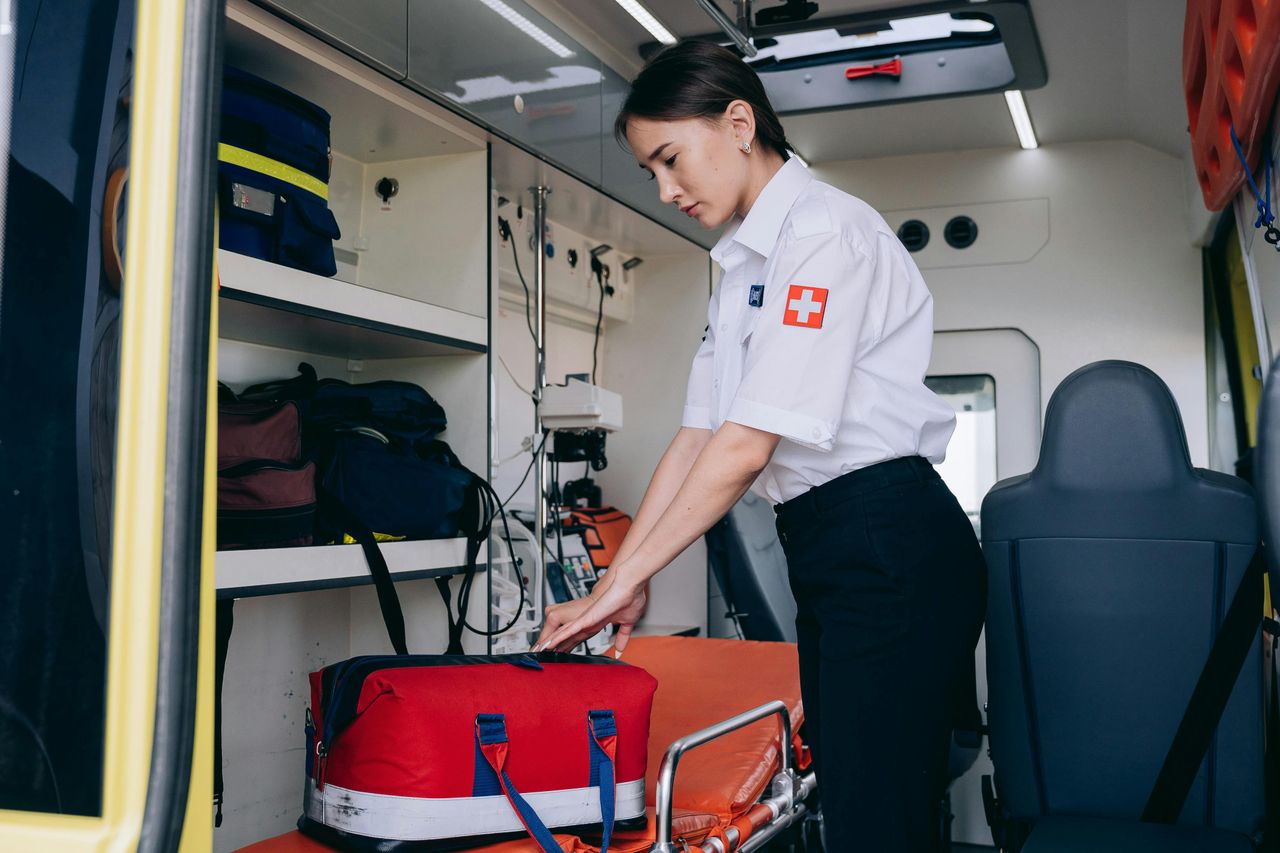 A female paramedic in uniform organizes medical supplies inside an ambulance with focused attention.